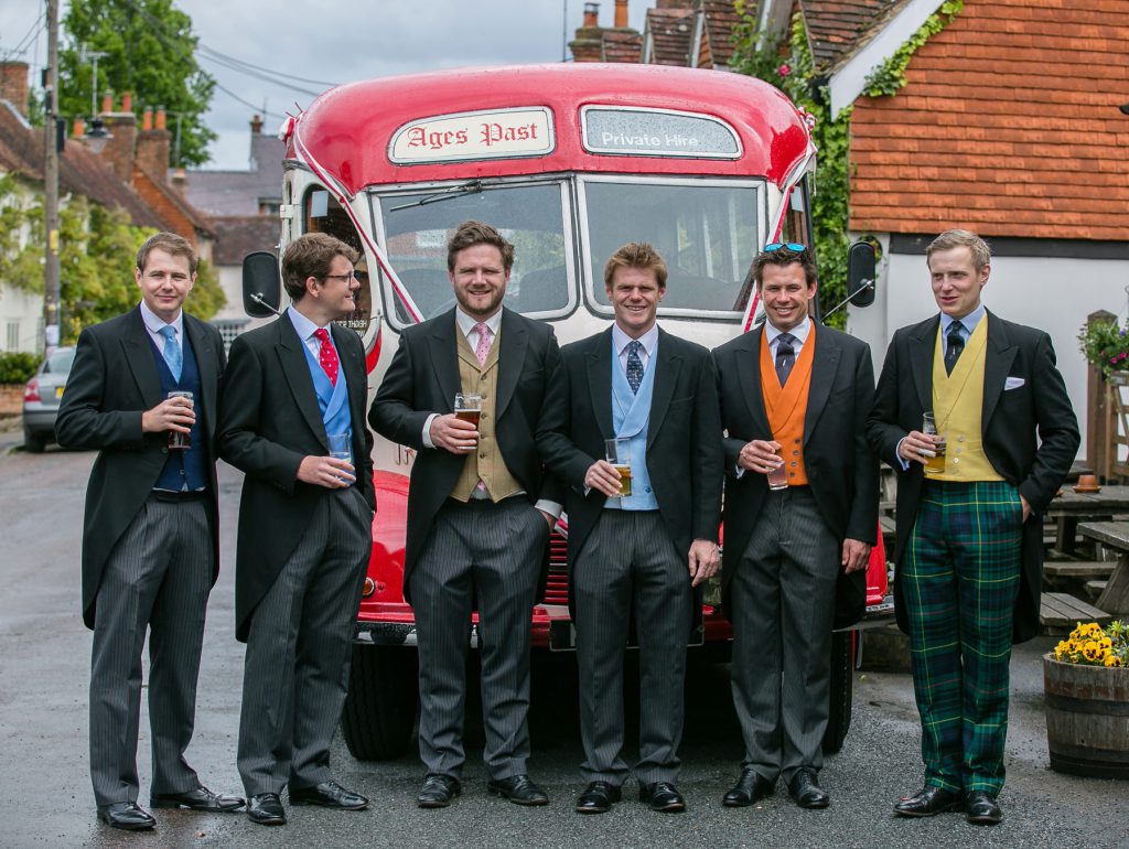 Groom and his best men standing in front of a bus with a pint of beer in their hands before going to church