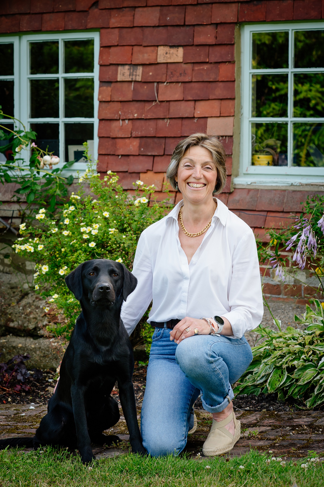contact me Anna kneeling with a black labrador sitting by her side