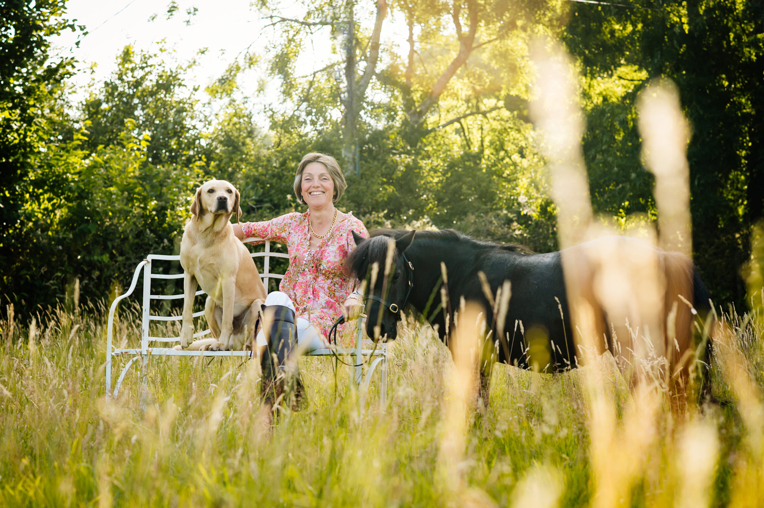 Anna sitting on a bench with her dog beside her and small pony standing
