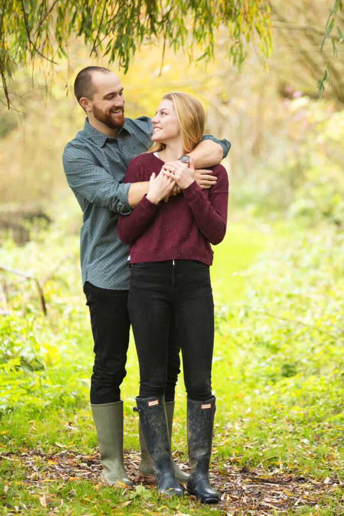 engaged coupling standing under a tree, smiling at each other