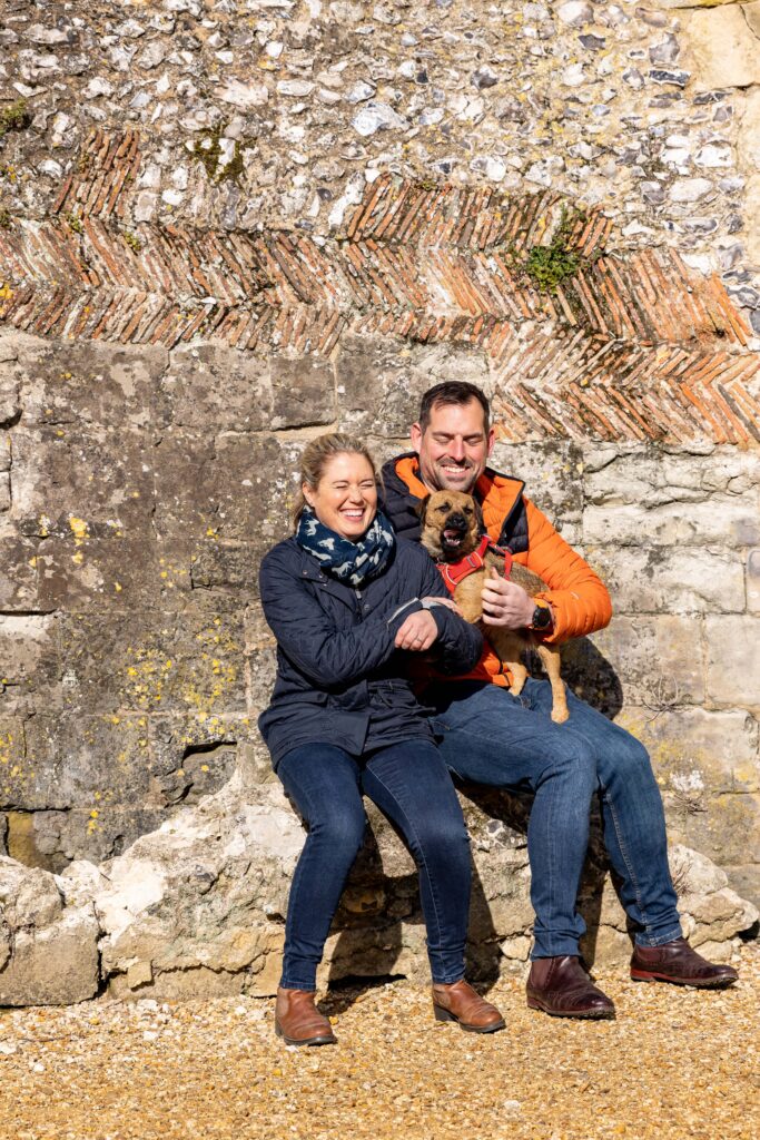 engaged couple sitting in the sunshine on a wall with their dog