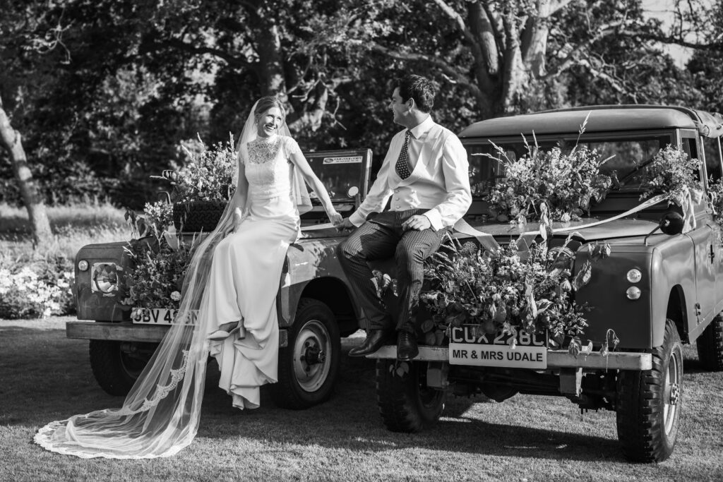 bride and groom sitting on their land rovers
