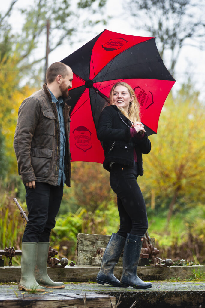 engaged couple on a bridge in the rain with an umbrella
