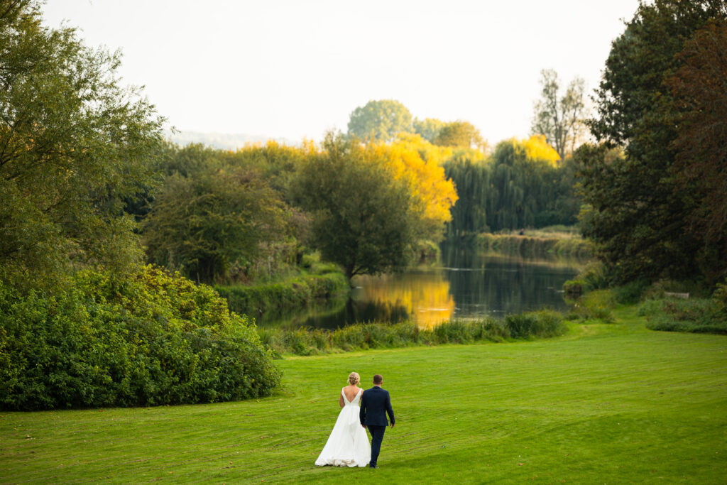 bride and groom walking down hill towards a beautiful river at golden hour