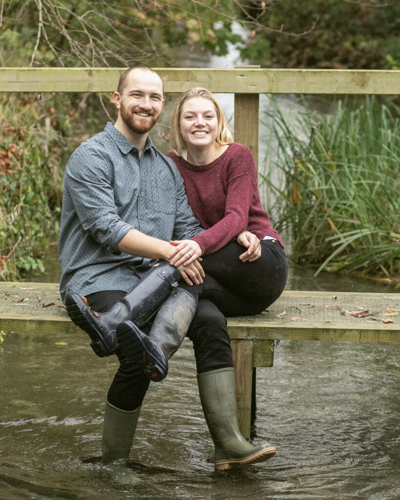 engaged couple sitting on a river bridge