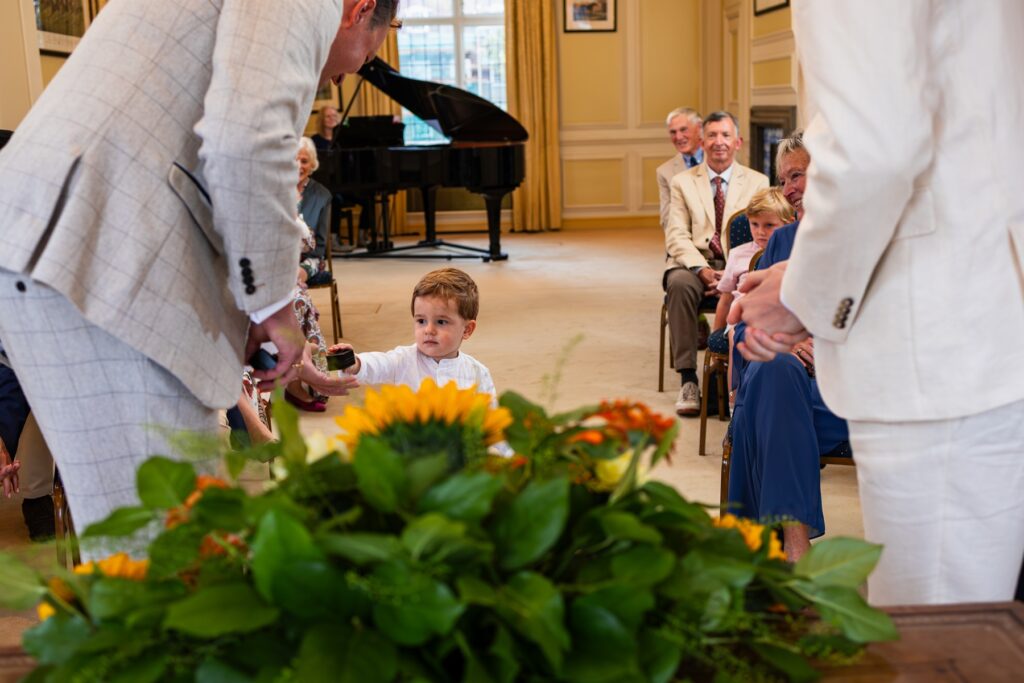Young boy bringing wedding ring up to the groom